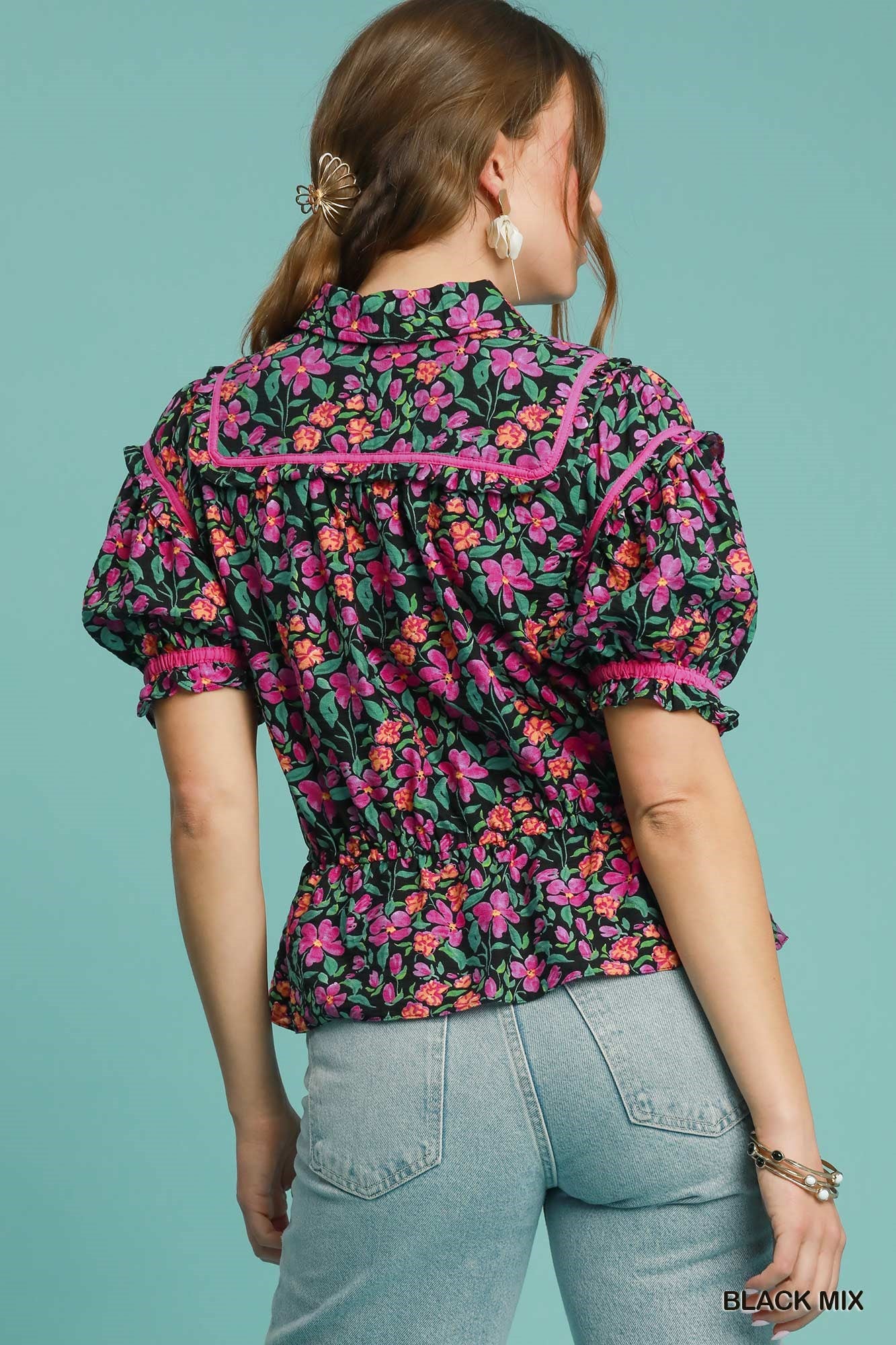 Woman wearing a floral blouse with pink accents against a teal background